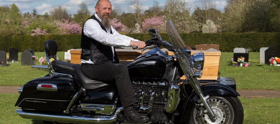 Man with beard sat on a motorbike at a funeral